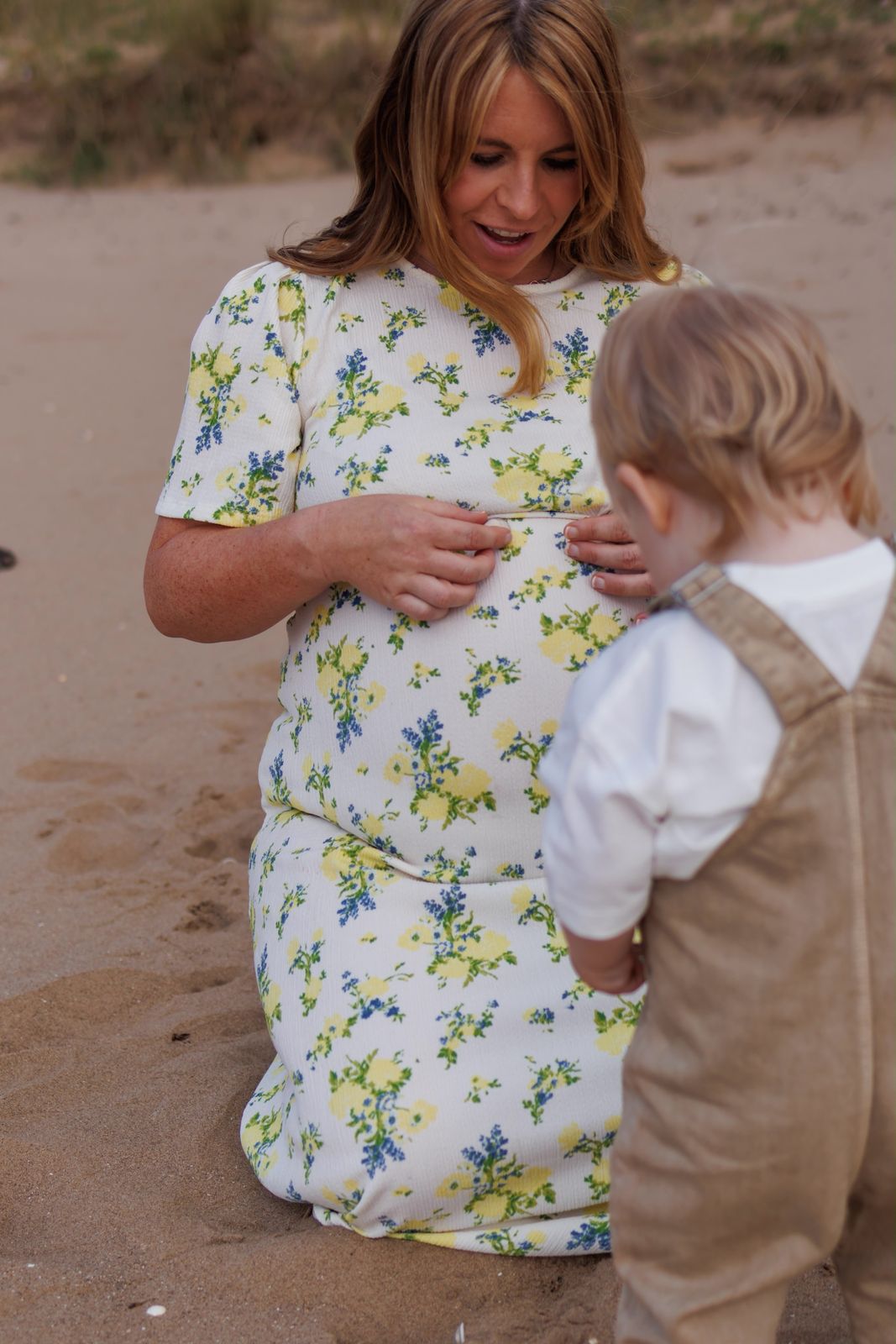 Mum-to-be in a floral dress with her toddler on the beach