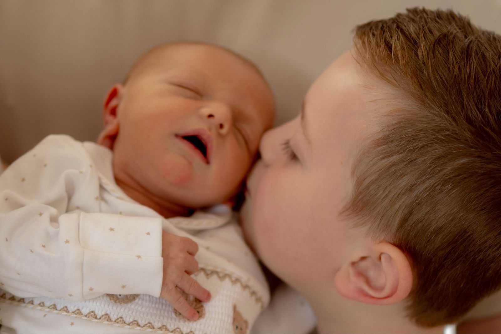 Big brother kissing his newborn sibling on the cheek