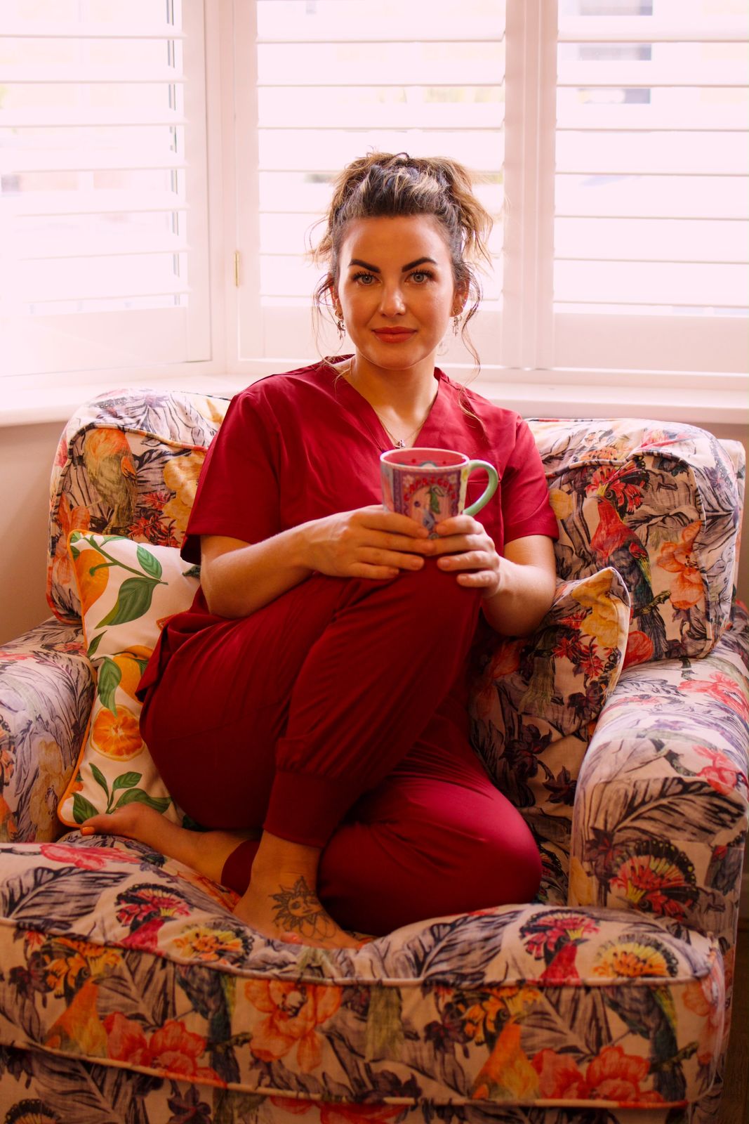 Beauty therapist in red scrubs relaxing in a floral armchair