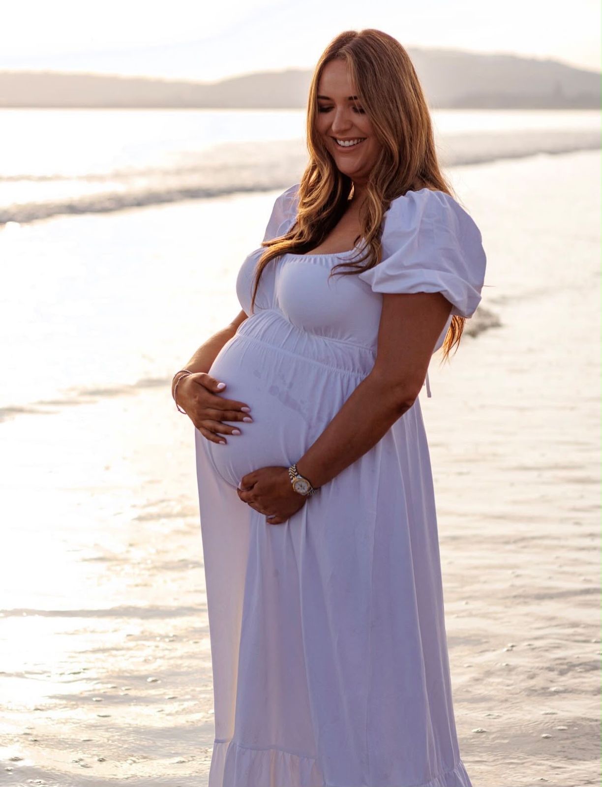 Mum-to-be in a white dress on the beach at sunset