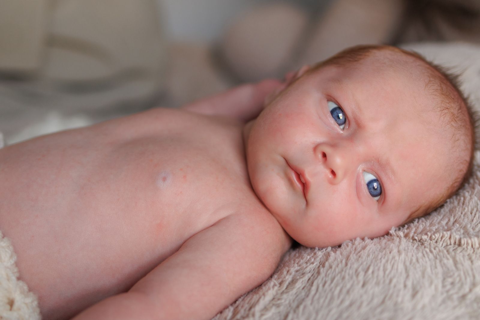 Newborn with bright blue eyes lying on a soft blanket