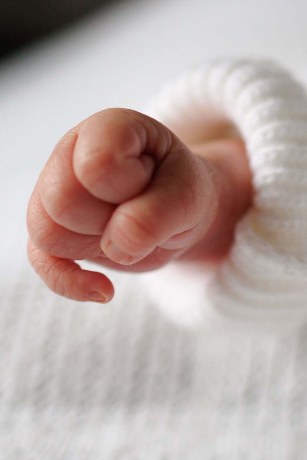 Close-up of a newborn's tiny fist in a white knitted sleeve