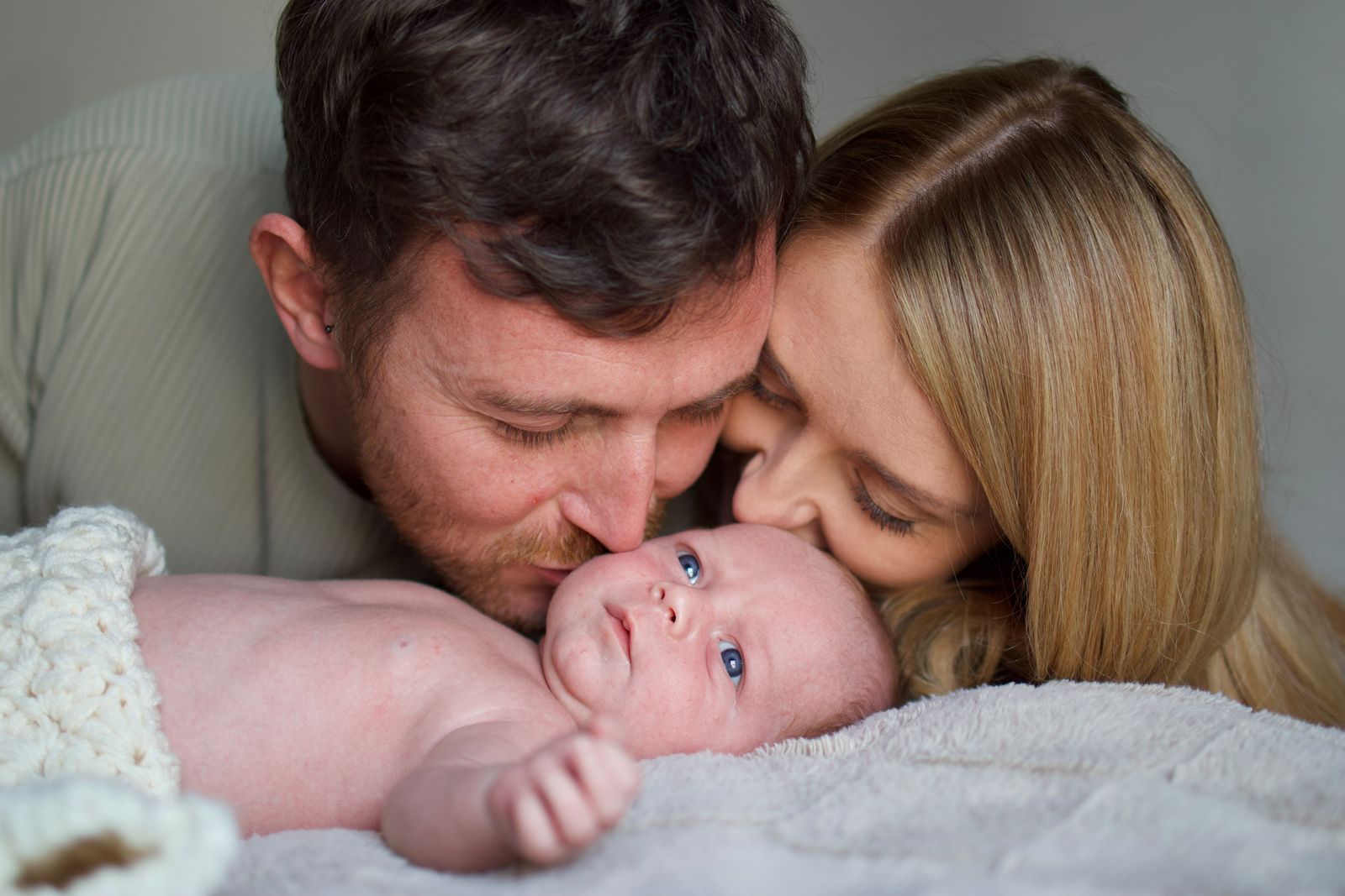 Parents kissing their baby lying on a soft blanket