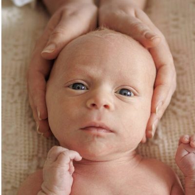 Newborn looking up, head cradled in a parent's hands